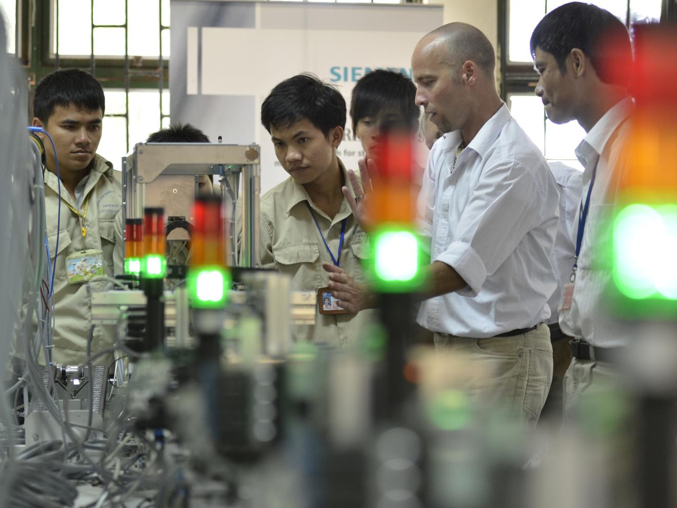 Eine Gruppe von Männern in Arbeitsbekleidung, die konzentriert auf eine technische Gerätschaft blicken.