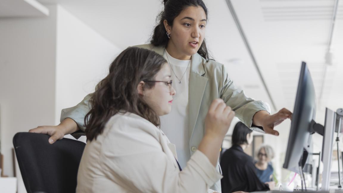 Eine Frau erklärt einer Mitarbeiterin etwas auf ihrem Computer