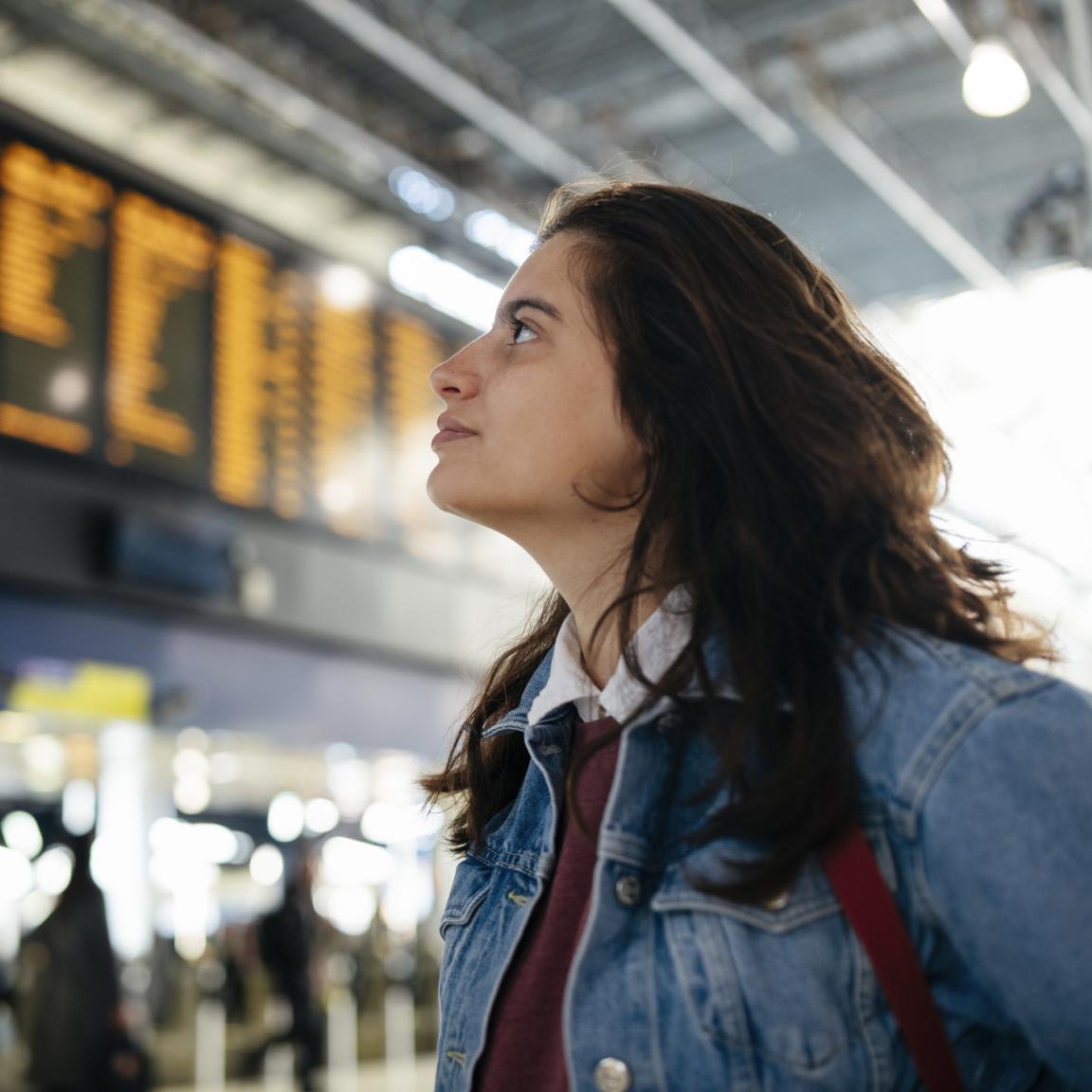 Frau prüft eine Abfahrtentabelle am Bahnhof